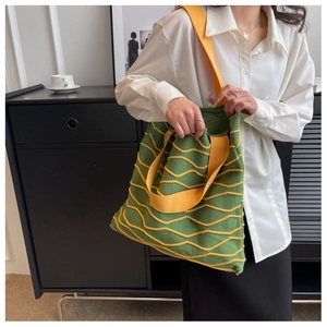 Detail of green knitted tote bag featuring yellow wavy texture and fabric shoulder strap