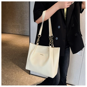 Close-up of cream tote bag with gold chain strap and fashion label on shoulder
