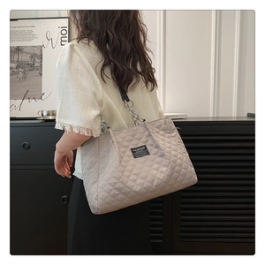 Detailed view of grey quilted tote bag with silver chain strap worn by a model