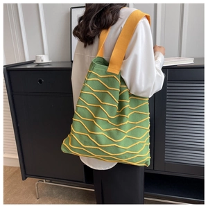 Detail of green knit tote bag featuring yellow wavy texture and wide shoulder strap