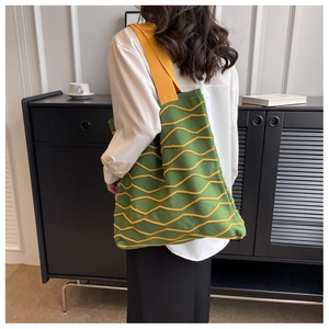 Detail view of a model wearing the green knit tote bag with yellow wavy textures