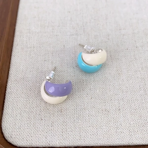 Minimalist C-shaped enamel stud earrings in purple and blue color contrast on beige fabric