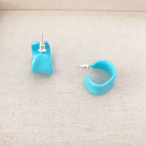 Macro detail of bright blue irregular C-shaped enamel earrings on soft beige fabric