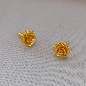 Elegant gold rose stud earrings with layered petals on soft textured fabric background