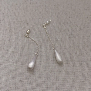 French minimalist silver brushed teardrop drop earrings on a rustic beige fabric background