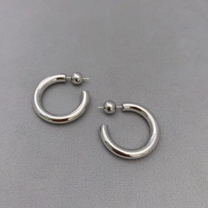 Detail of silver C-shaped hoop earrings with ball ends on a textured gray background