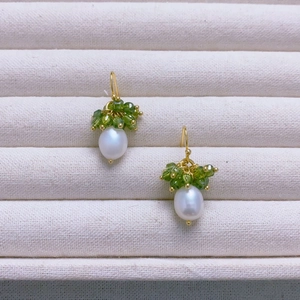 Close-up of handmade pearl drop earrings with green crystal beads and gold hooks