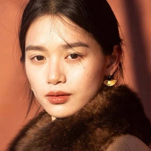 Elegant gold fan earrings with black beads worn by a model in soft lighting
