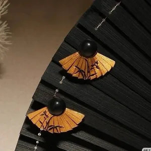 Detail view of gold fan earrings with bamboo engraving and elegant black pearl accents