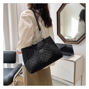 Detail of black quilted nylon tote bag with a chain strap and fashion label on the front