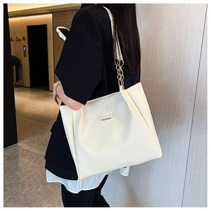 Detail of cream white tote bag featuring gold chain strap and fashion label on shoulder