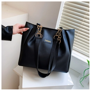 Detail of black leather tote bag featuring gold chain link handles and FASHION logo plaque