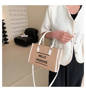 Détail d'un sac cabas kaki avec texte HELLO WEEKEND et bordure blanche sur un canapé