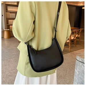 Detail of a black leather crescent hobo bag with embossed lettering on green blazer
