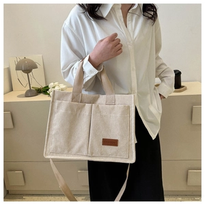 Detail of off-white corduroy tote bag with double front pockets and brown logo tag