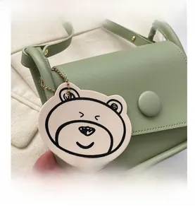 Close-up of light green PU leather saddle bag with round buckle and cute bear charm