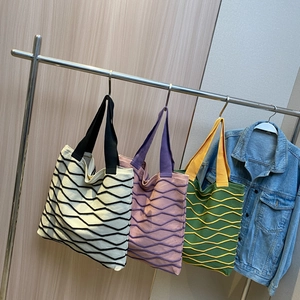 Three colorful wavy knit tote bags with wide handles hanging on a rack for daily use