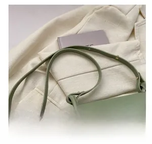 Detail view of avocado green saddle bag with bear charm on tweed jacket background