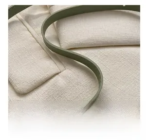 Detail of sage green leather strap and off-white woven fabric on crossbody saddle bag