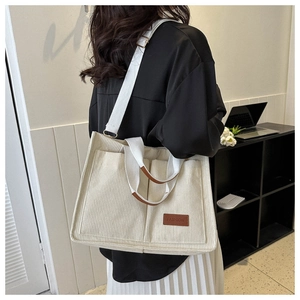 Detail showing the creamy white corduroy tote bag texture and fashion leather tag