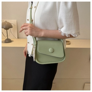Detail of light green leather saddle bag featuring a unique asymmetrical curved flap design