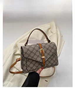 Detail of dark grey handbag with clover pattern and brown leather straps on model