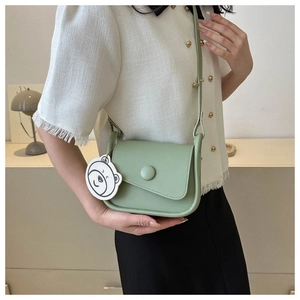 Detail of light green saddle bag with bear tag worn as a cross-body shoulder bag