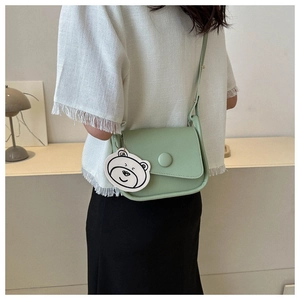 Detail of light green crossbody bag with cute bear pendant in a minimalist setting