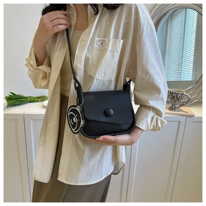 Detail of a black leather saddle bag featuring a cute panda charm and round buckle closure