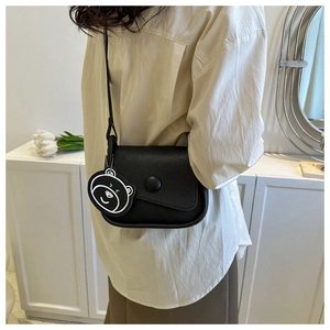 Close-up of black matte leather saddle bag with round buckle and cute bear charm