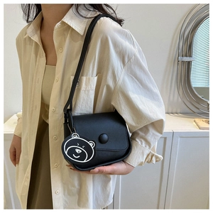 Close-up of black leather saddle bag with round buckle and cute bear charm detail