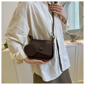 Detail of dark brown retro leather crossbody bag with adjustable strap and bear charm