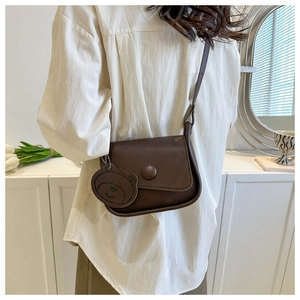 Detail of a brown vintage saddle bag with a cute bear charm and rounded flap design