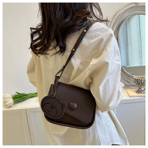 Detail of dark brown leather saddle bag with bear charm and adjustable strap for women