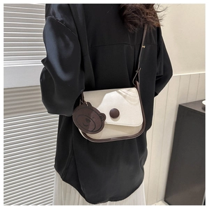 Detail view of contrast stitch saddle bag with cute bear charm and round buckle detail