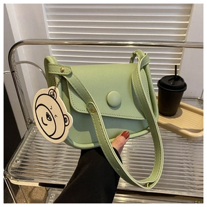 Close-up of light green crossbody saddle bag featuring a cute cartoon bear pendant