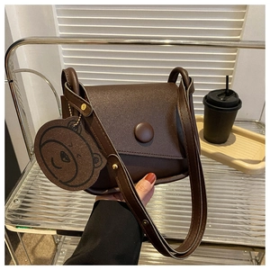 Detail of a dark brown PU leather saddle bag with round closure and bear charm
