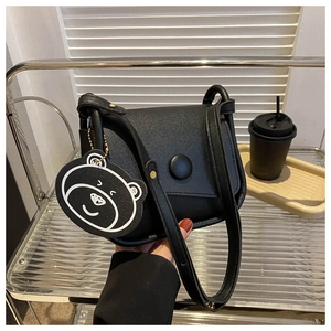 Detail of black matte saddle bag featuring a large round buckle and cute bear pendant