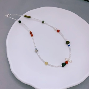 Collana boho con pietre naturali multicolori e perle barocche su un piatto di ceramica bianca
