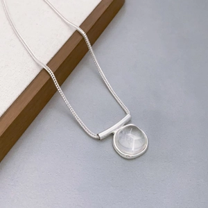 Macro detail of a silver necklace featuring a round translucent white crystal pendant