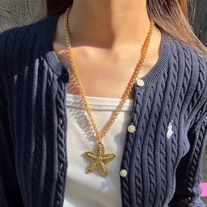 Collier à grosse chaîne dorée avec pendentif étoile de mer texturé porté sur un pull