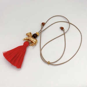 Detail of a golden zebra pendant with vibrant red tassels and a beaded woven necklace cord