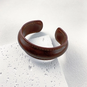 Vintage brown genuine leather cuff bracelet with yellow stitching on stone pedestal