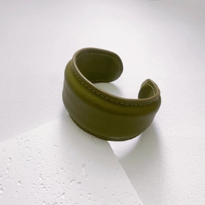 Detail of olive green leather cuff bracelet with visible stitching on a stone display