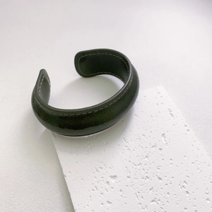 Close-up of dark green vintage leather cuff bracelet with detailed stitching on stone base