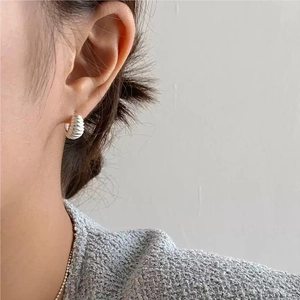 Detail of silver-toned croissant hoop earring with spiral texture on female model