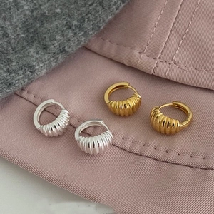 Pair of gold and silver croissant dome hoop earrings with ribbed texture on fabric background