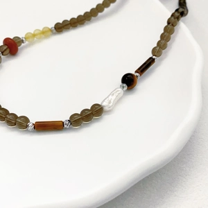 Handmade necklace featuring baroque pearls, tiger eye stones, and citrine beads on white tray