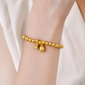 Dettaglio del bracciale di perle in oro opaco con eleganti ciondoli a loto e baccello