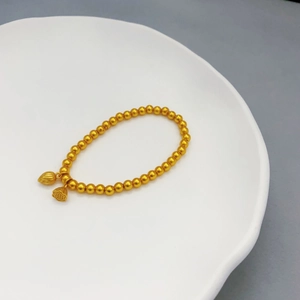 Elegante bracciale a sfere dorate con ciondoli a loto e seme su un piatto di ceramica